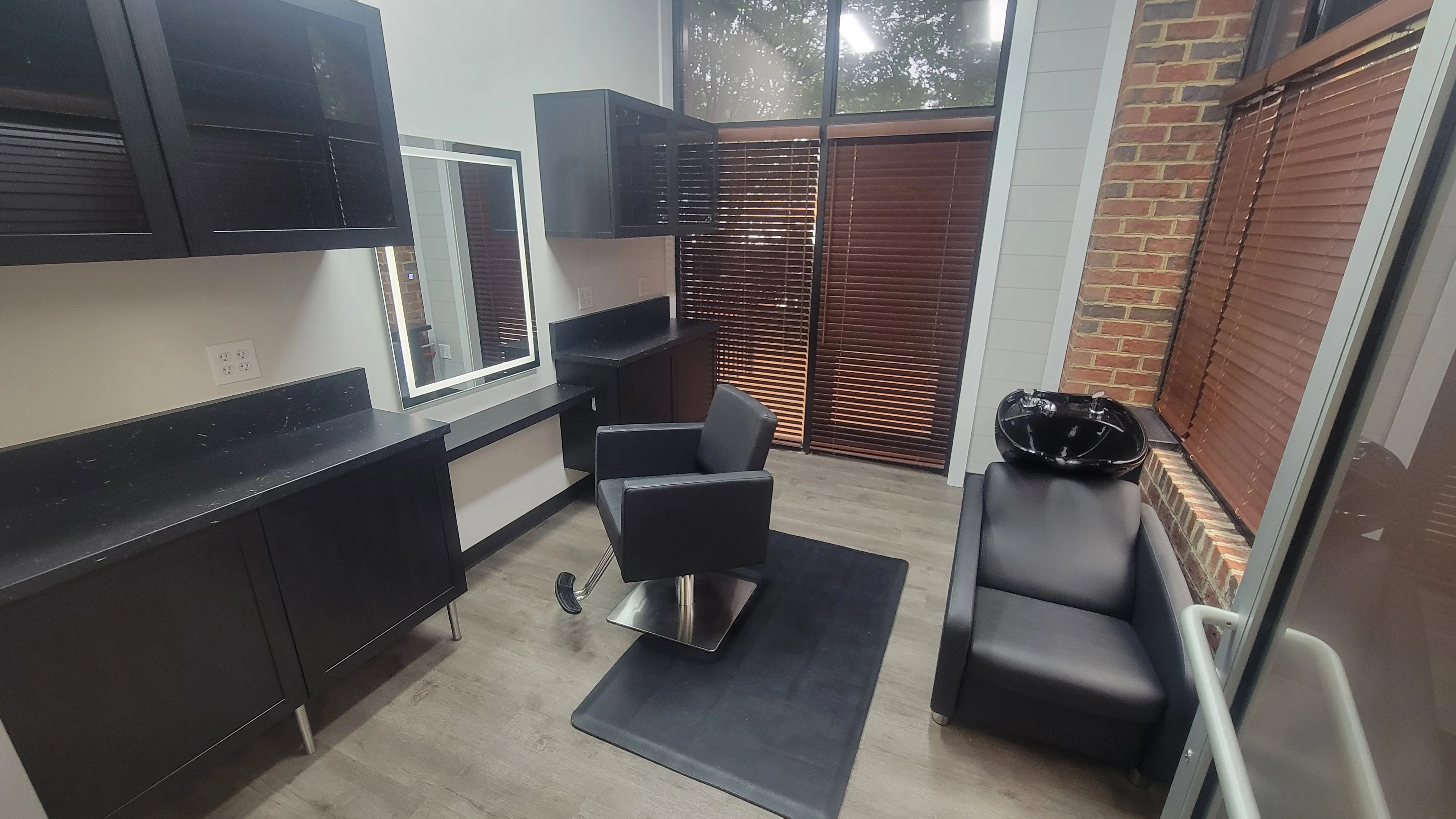 A window suite with styling station, mirror, shampoo bowl, and exposed brick